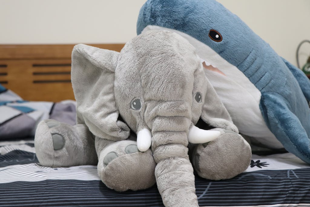 Cute plush elephant and shark toys sitting together on a bed, creating a cozy childhood feel.