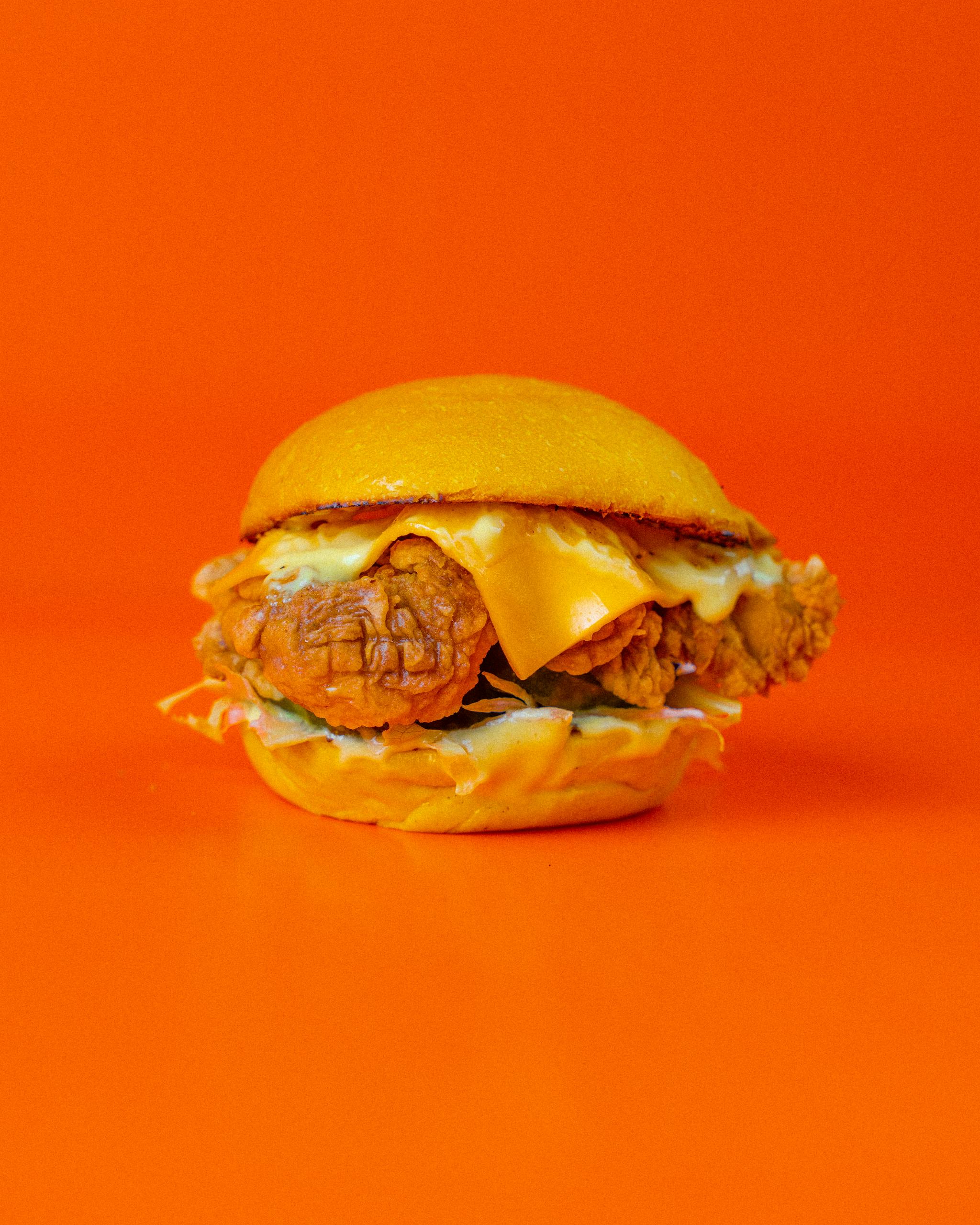 Delicious chicken burger with cheese on orange background, perfect for fast food themes.