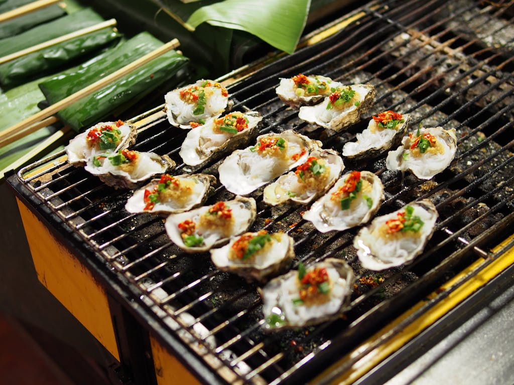 Delicious grilled oysters with spicy chili and herbs on a barbecue grill, perfect for seafood lovers.