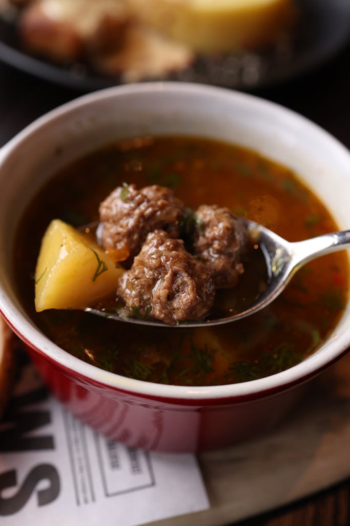 Delicious meatball soup with potatoes in a red bowl, ideal for cozy meals.