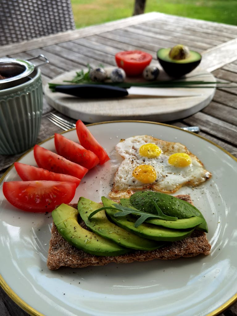 Delicious outdoor breakfast featuring avocado toast, quail eggs, and fresh tomatoes, perfect for a nutritious start to the day.