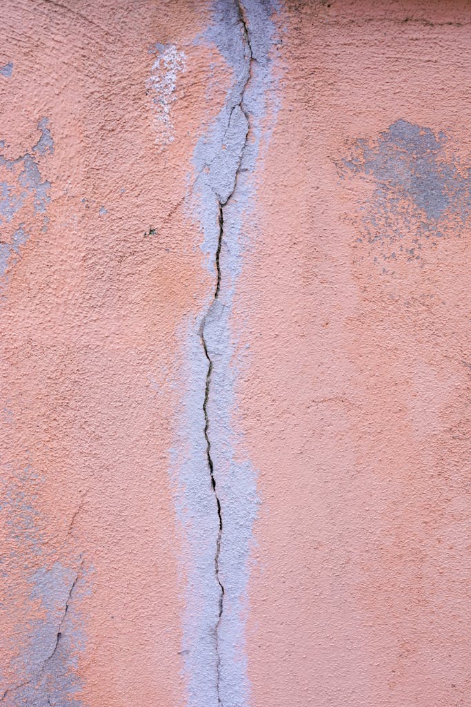 Detailed close-up of a pink plaster wall with visible cracks, ideal for backgrounds.