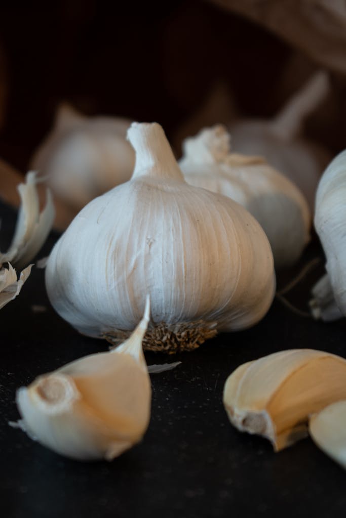 Detailed close-up of fresh organic garlic bulbs and cloves on a dark background, perfect for food blogs.