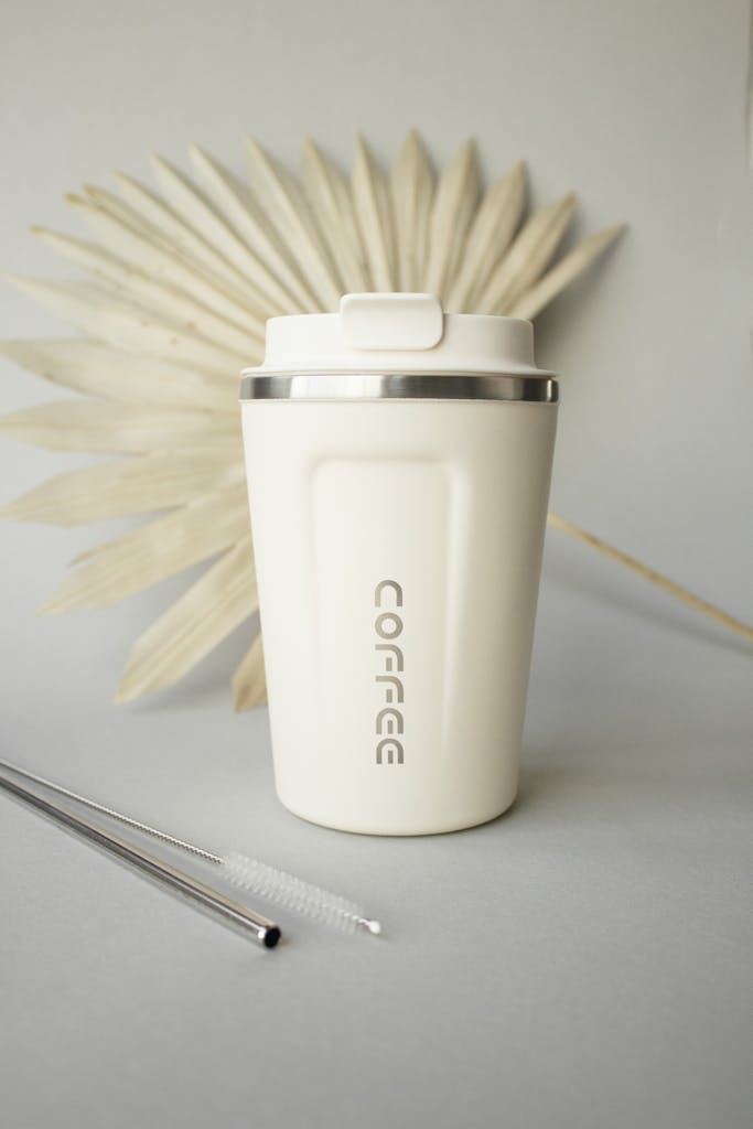 Elegant beige coffee tumbler with metal straws and palm leaf, perfect for modern coffee enthusiasts.