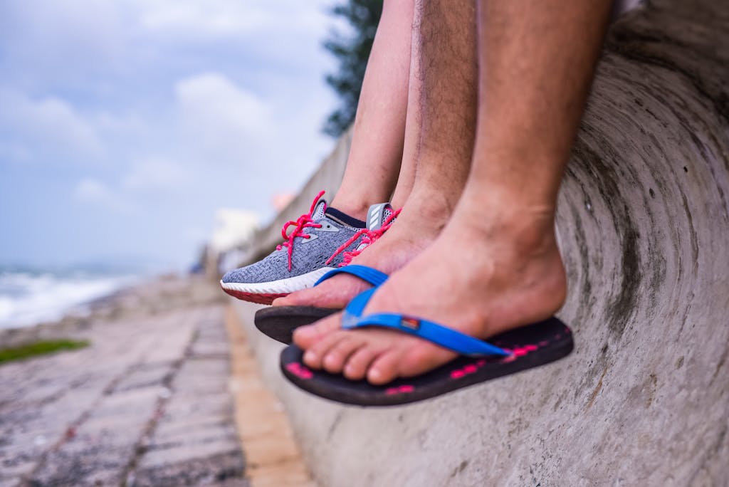 Feet in sneakers and flip-flops resting on a seaside wall with ocean view.