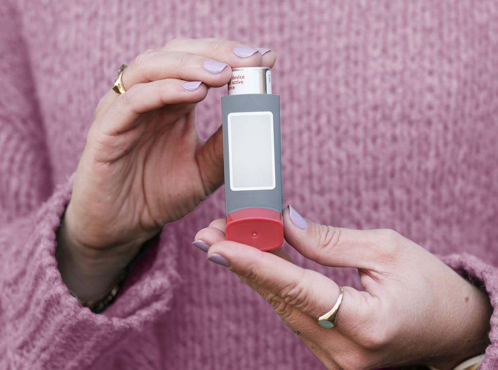Female hands holding an asthma inhaler with a pink sweater background.