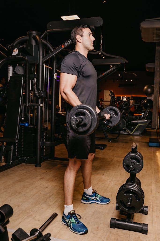 Fit adult man in gym performing weightlifting workout with dumbbells.