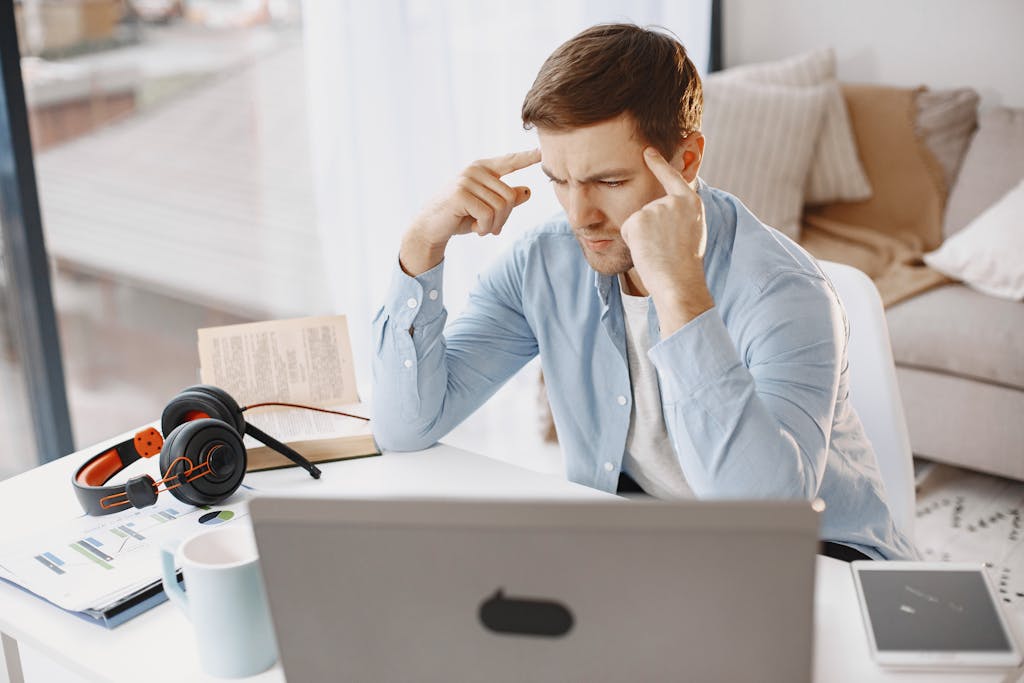 Focused man working remotely on his laptop in a cozy home setting, surrounded by work materials.