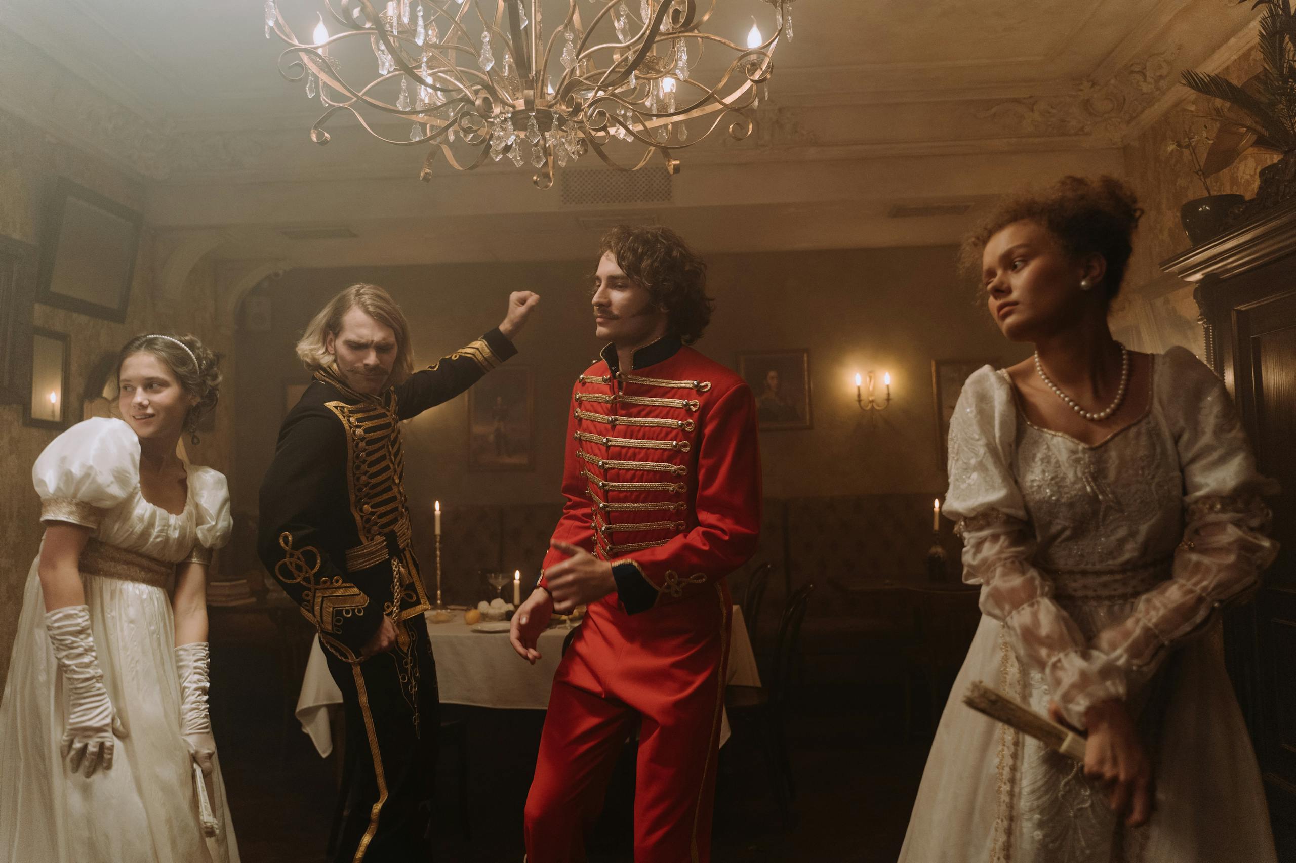 Four adults dressed in Regency-style attire dance in an elegant indoor setting.