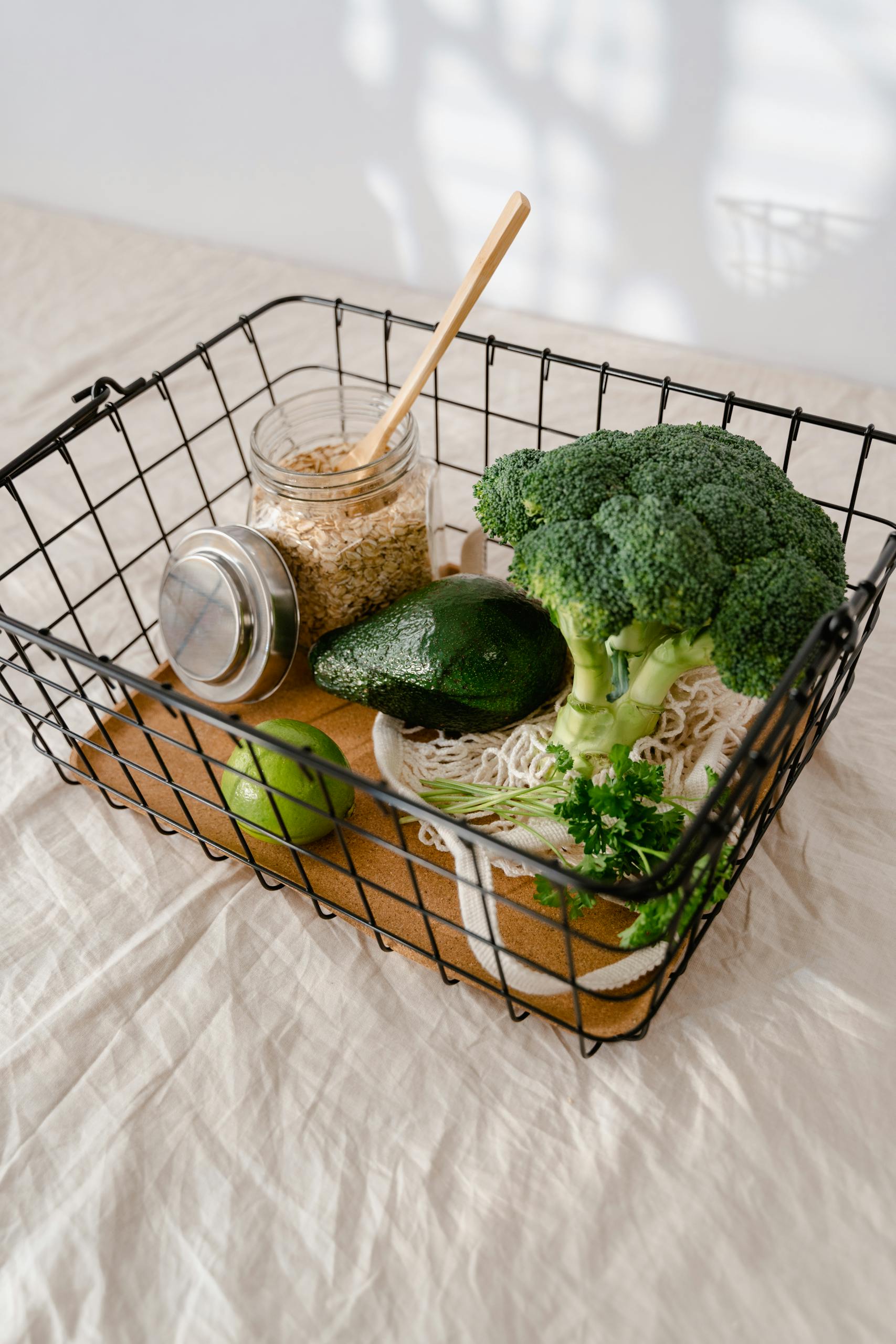 Fresh broccoli, avocado, and oats ready for healthy meal preparations in a wire basket.