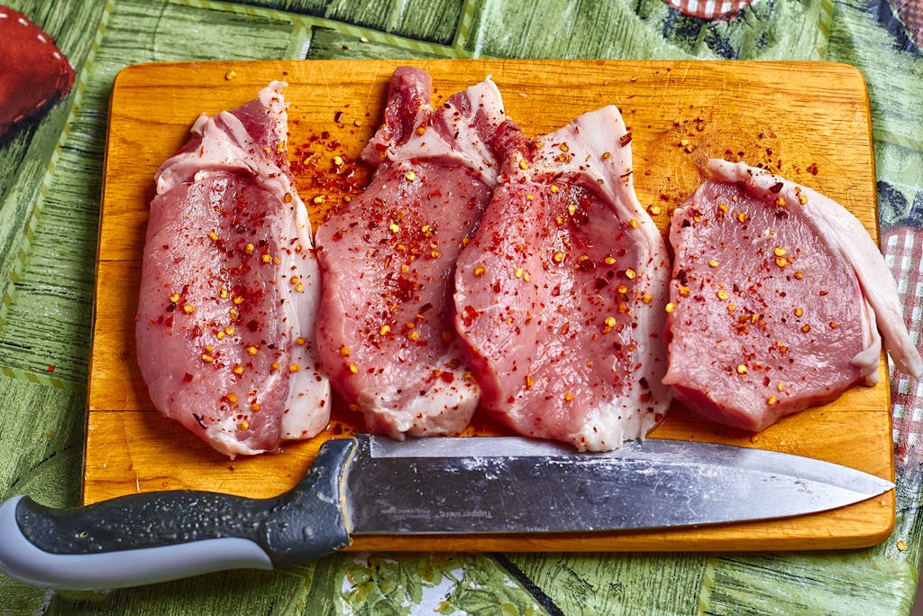 Freshly seasoned pork chops with spices on a wooden chopping board, ready for cooking.