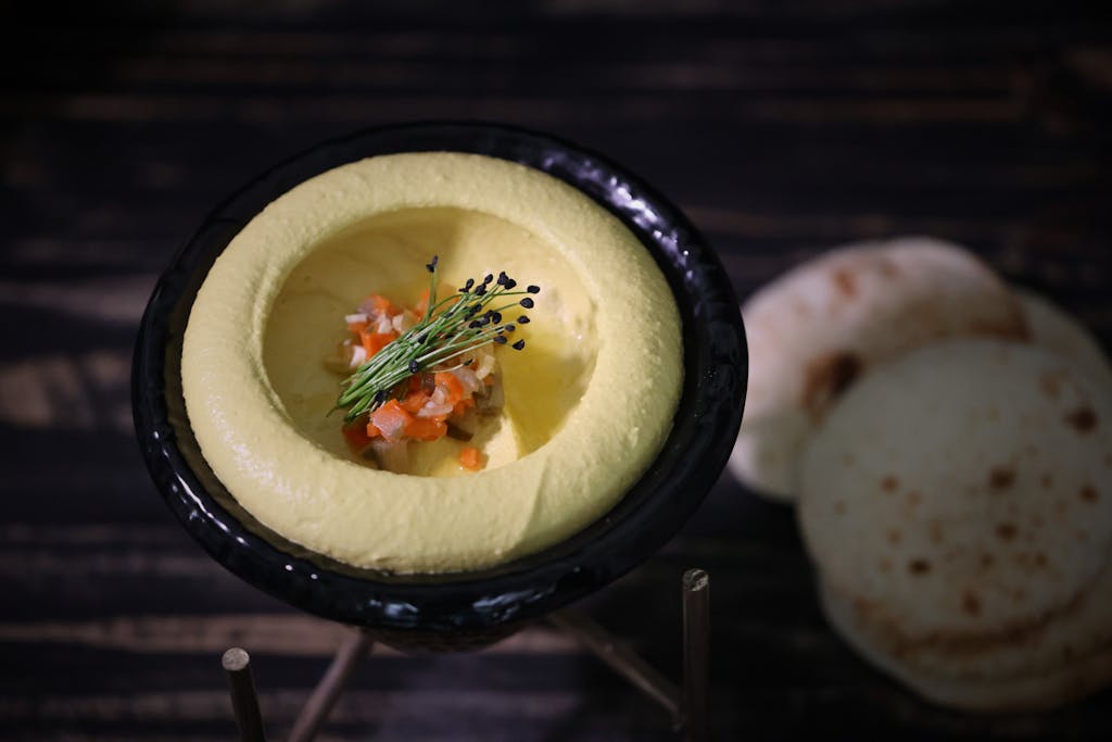 Gourmet hummus elegantly presented in a black bowl garnished with herbs and vegetables.