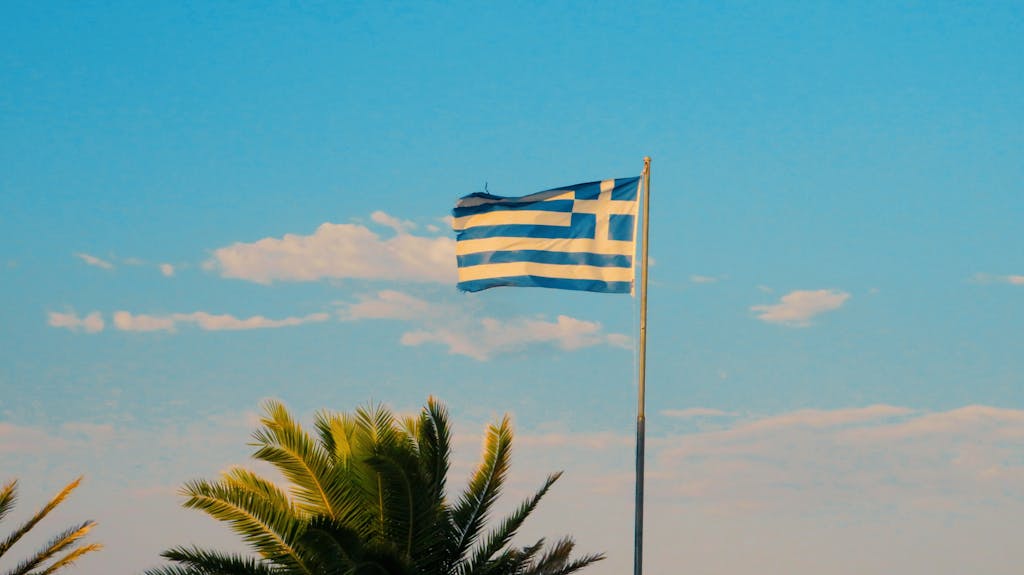 Greek flag waving prominently against a clear blue sky, symbolizing national pride.