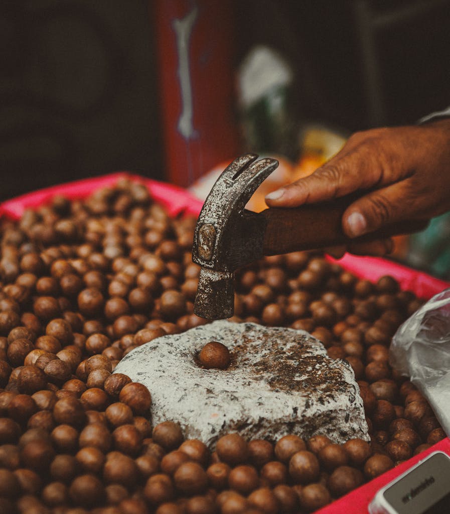 Hand cracking macadamia nuts with a hammer in São Paulo, highlighting local market culture.