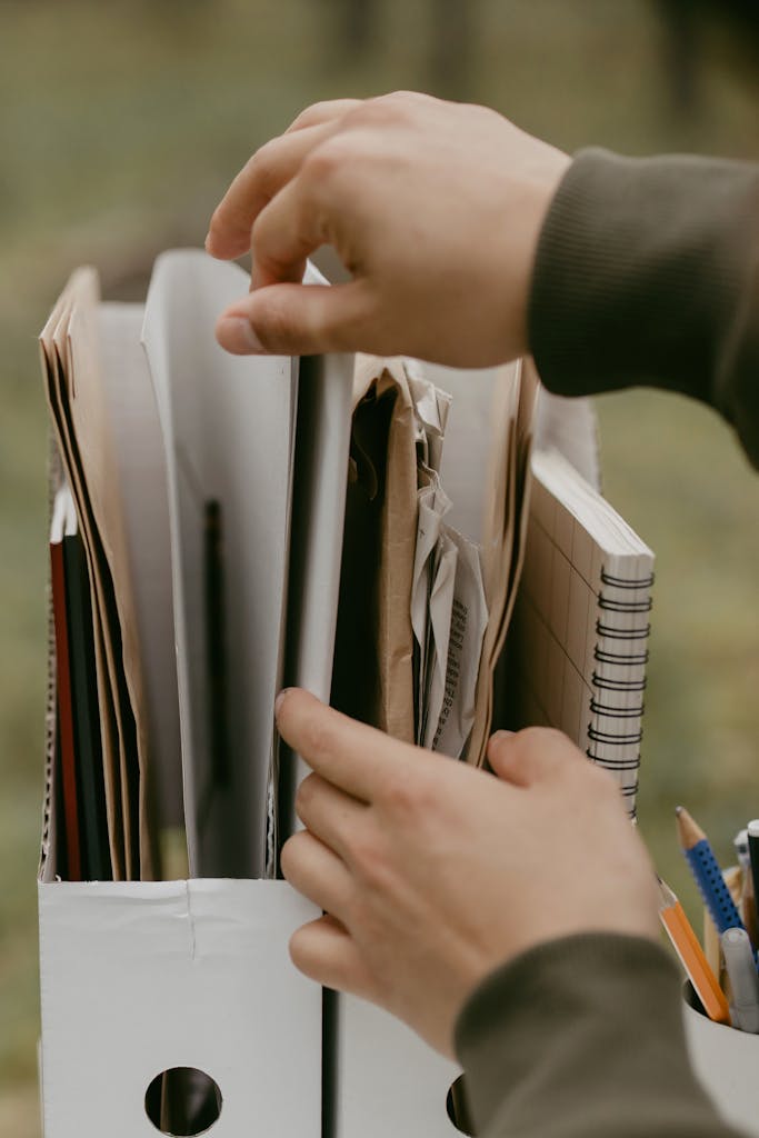 Hands arranging papers and notebooks in a box, highlighting organization and office work.