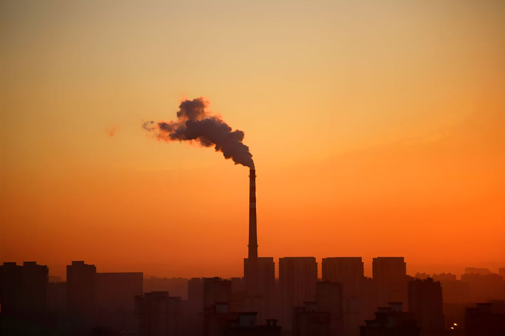 Industrial smokestack emitting smoke during sunset, highlighting environmental impact.