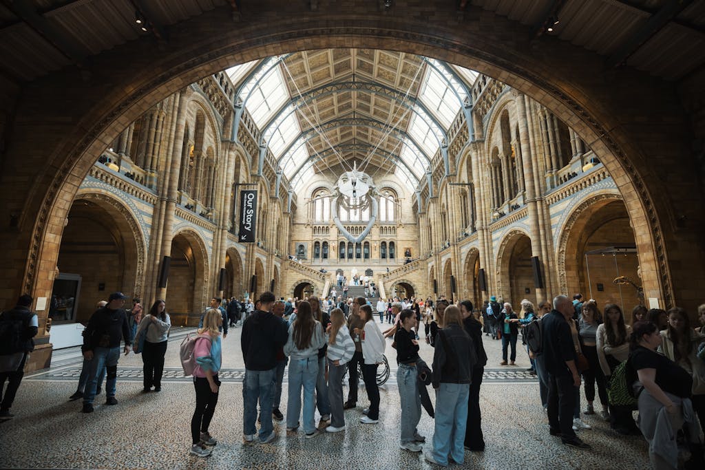 Inside the bustling Natural History Museum with a diverse crowd. Ornate architecture in a bright, dynamic setting.