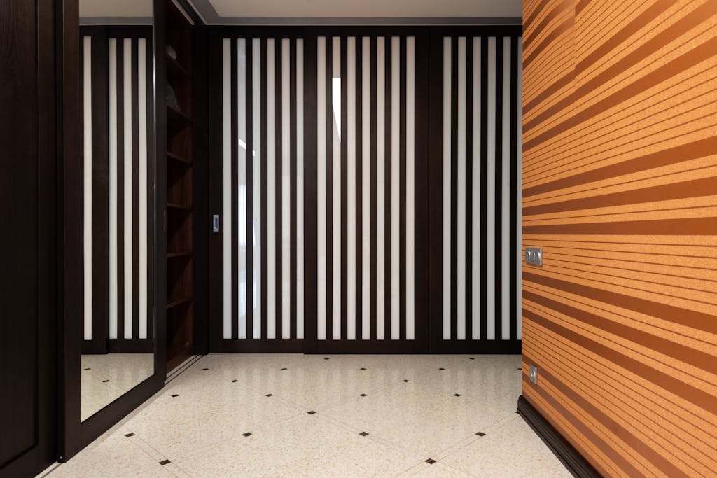 Interior of modern hallway with mirror and black striped decor and orange wall in apartment with tiled floor at home