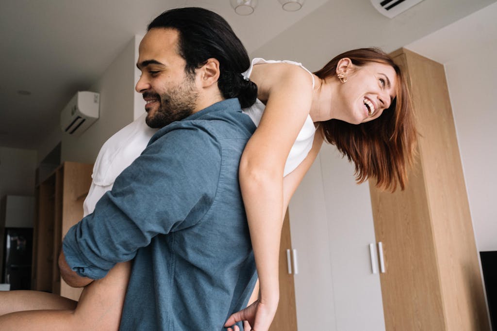 Joyful couple laughing together indoors, enjoying playful moment in a cozy home setting.