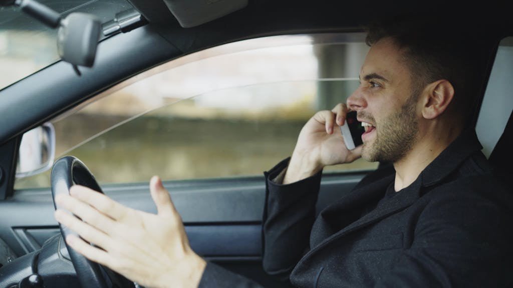 Man in car talking on cell phone while driving, displaying frustration