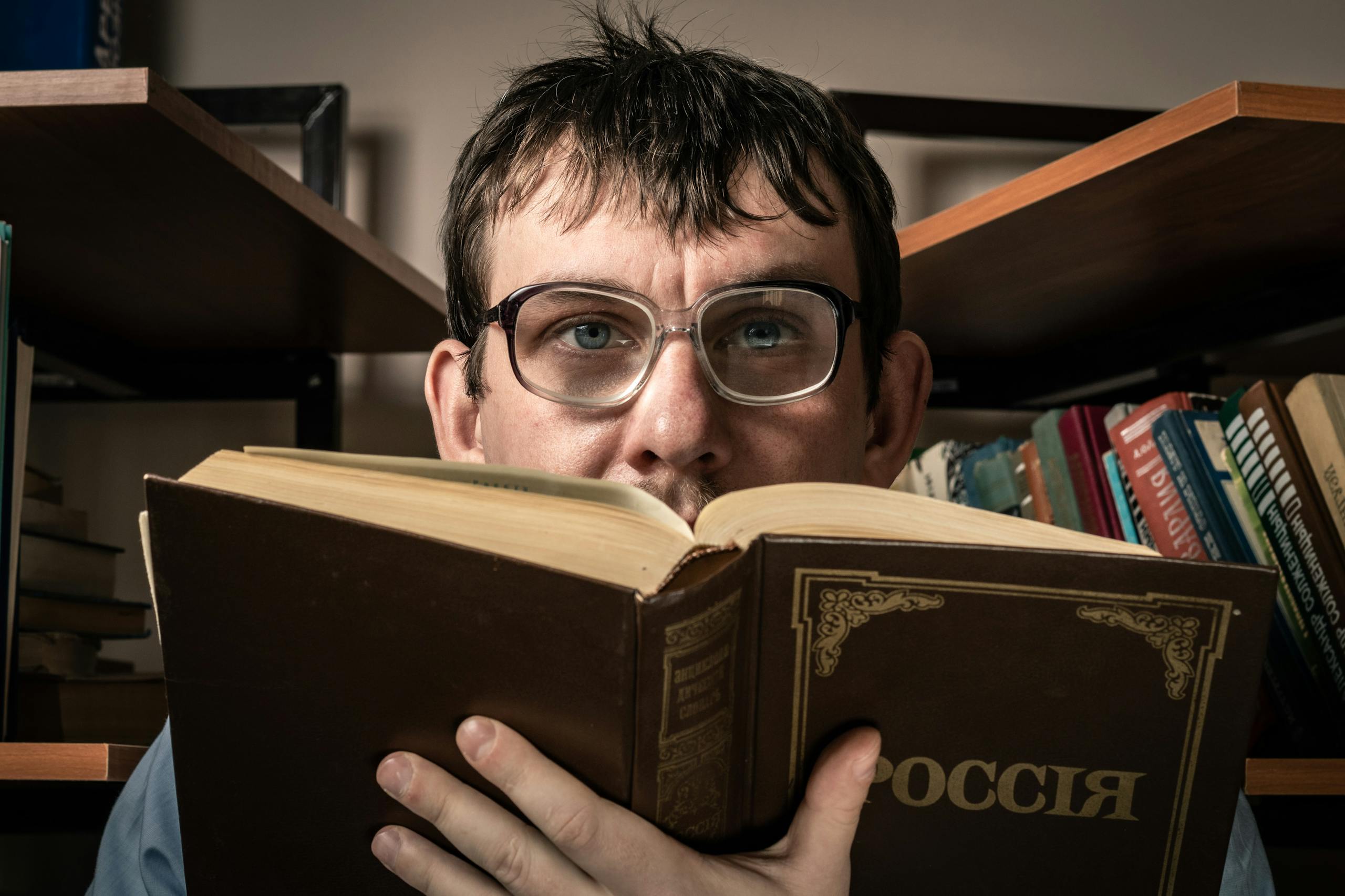Man with glasses reading a book titled 'Россия' in a cozy library setting.