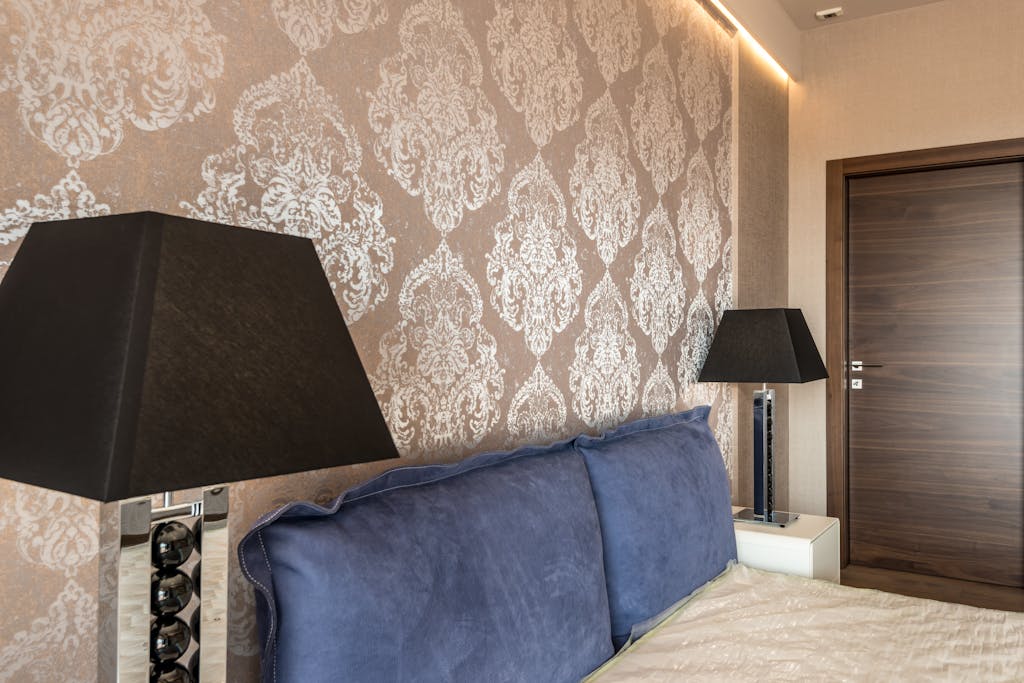 Modern bedroom with elegant wallpaper design, blue pillows, and stylish black lamps.