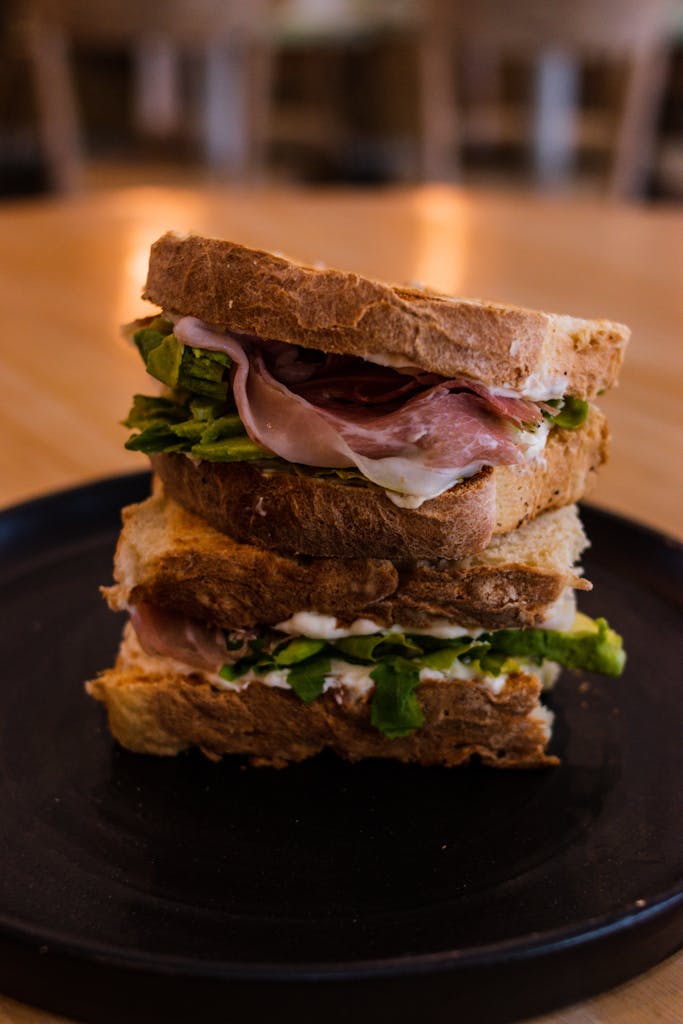 Mouth-watering stack of fresh ham, lettuce, and bread on a black plate.