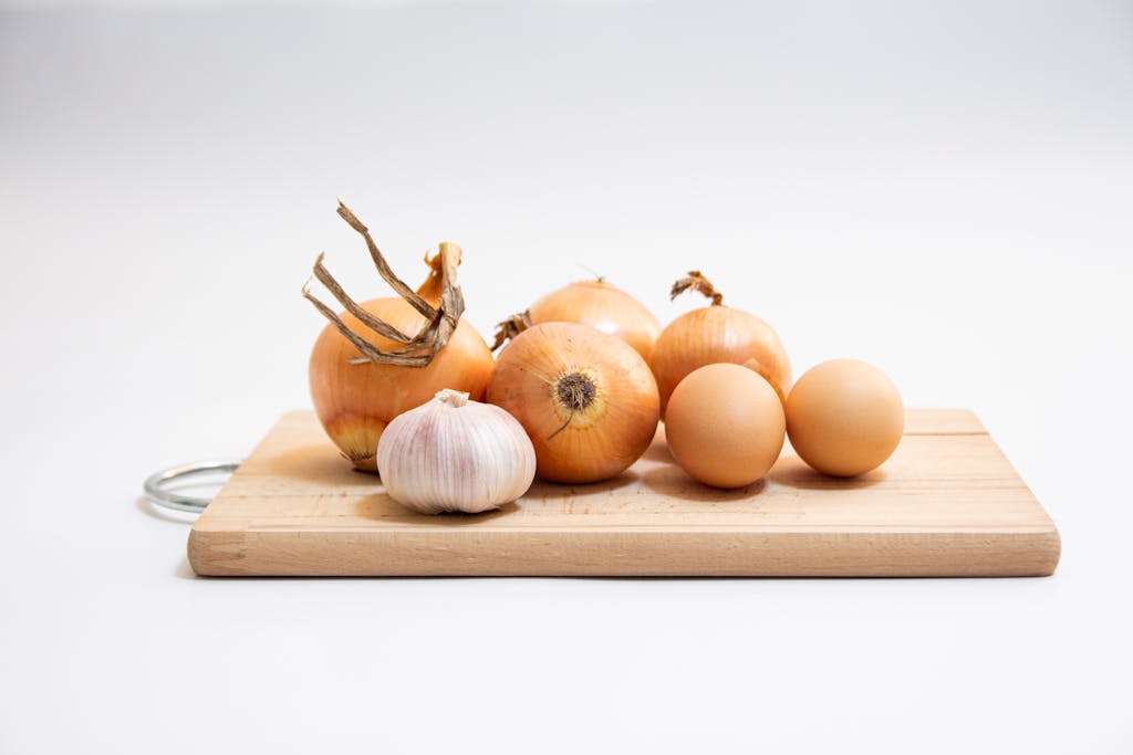 Organic onions and garlic cloves arranged on a wooden cutting board in a minimalist kitchen setting.