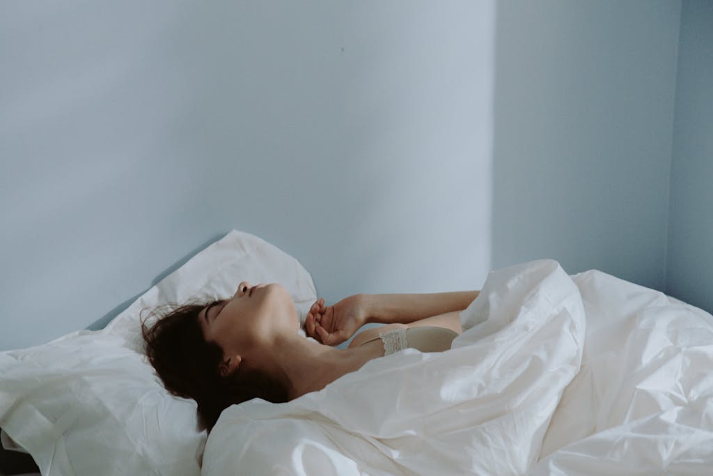 Peaceful scene of a woman sleeping in a soft bed with white linens indoors.