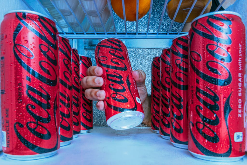 Person grabbing a cold soda can from a stocked refrigerator interior.