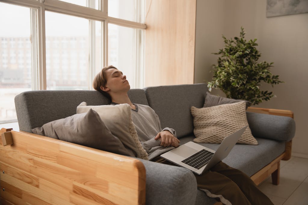 Person relaxing on a sofa indoors with a laptop, enjoying a peaceful moment.