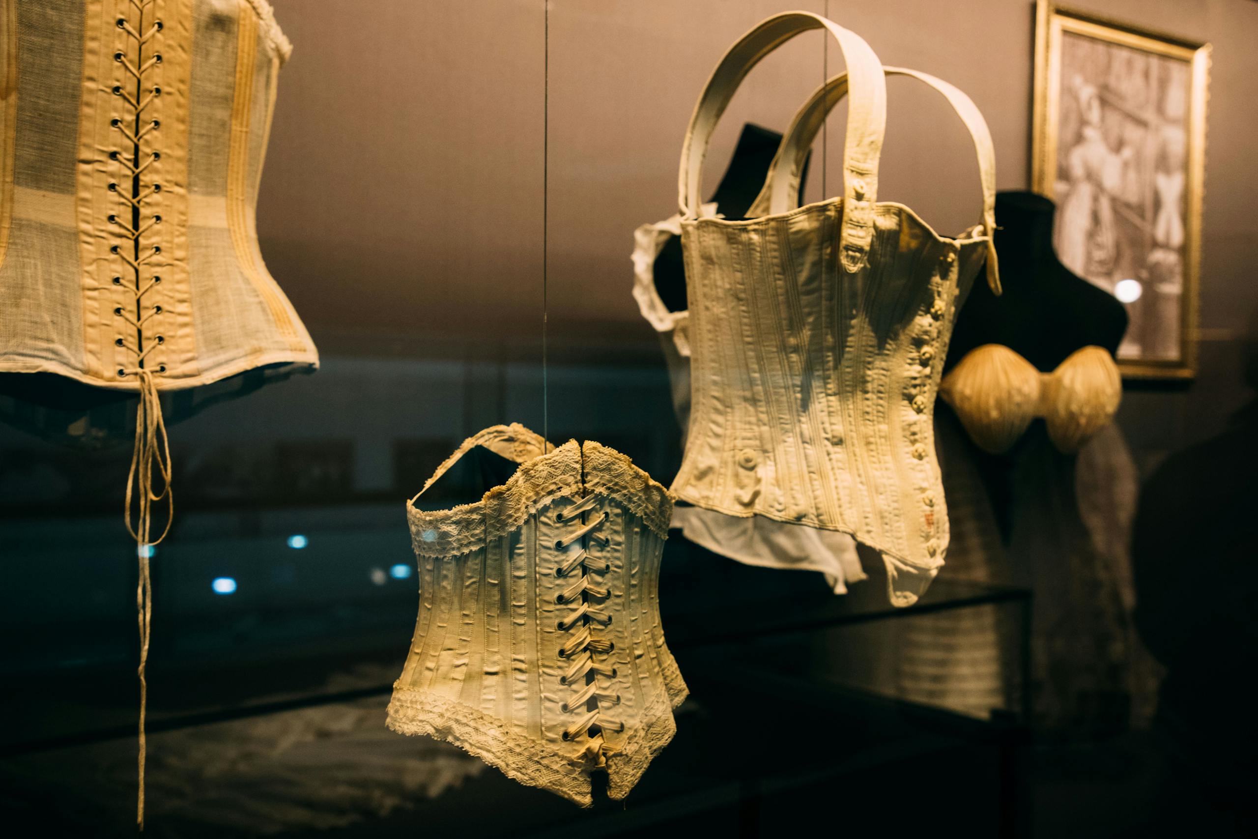 Showcase with collection of historical corsets with laces near picture on wall on exhibition