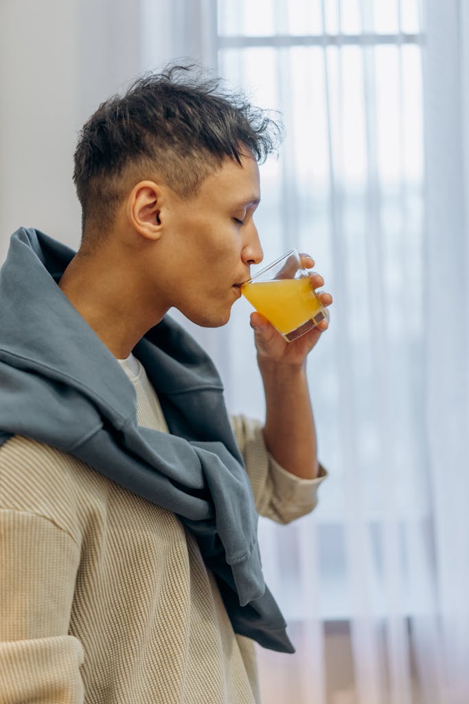 Side view of a man drinking fresh juice indoors, eyes closed savoring the taste.