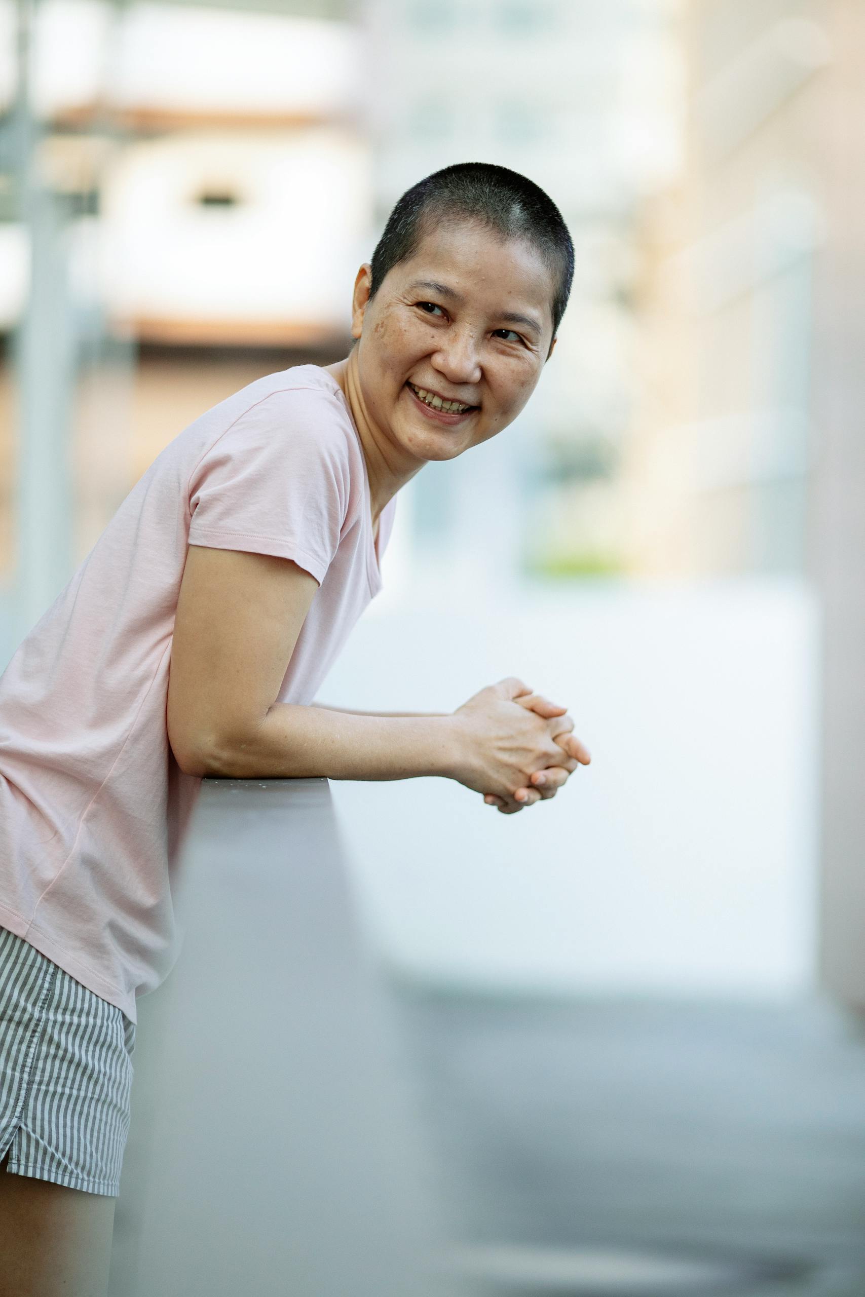 Side view of happy sick ethnic female smiling and looking away on balcony of hospital on blurred background