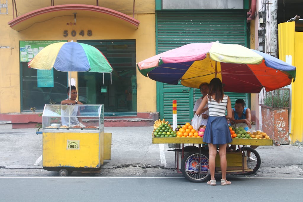 Street vendors selling fruits under colorful umbrellas in an urban setting.