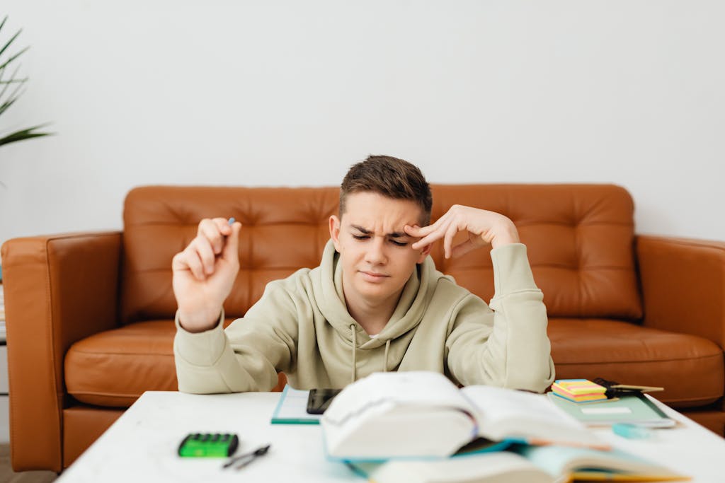 Teenage boy studying on a brown sofa, focused and thinking hard indoors.