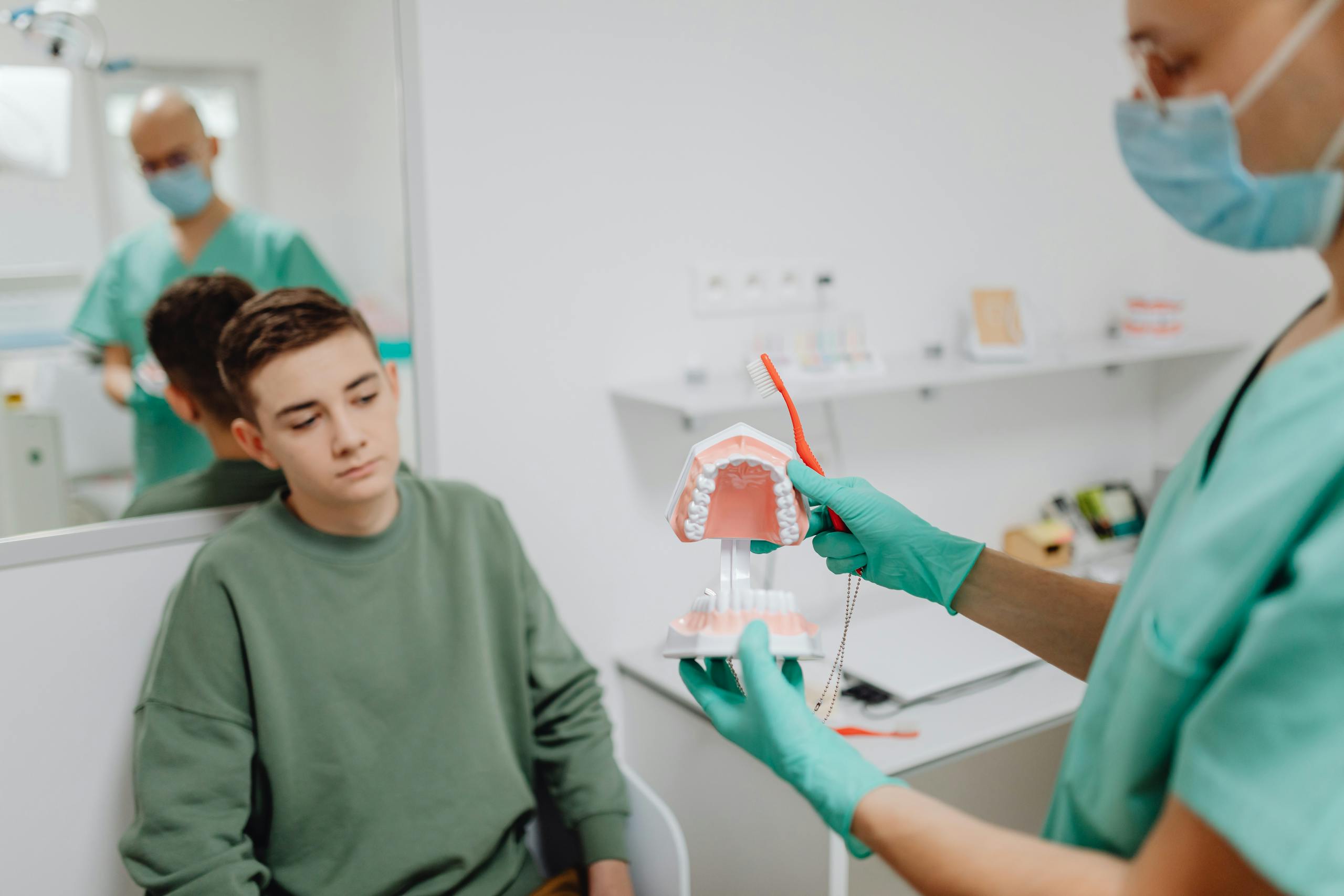 Teenager learning dental hygiene from dentist using a dental model.