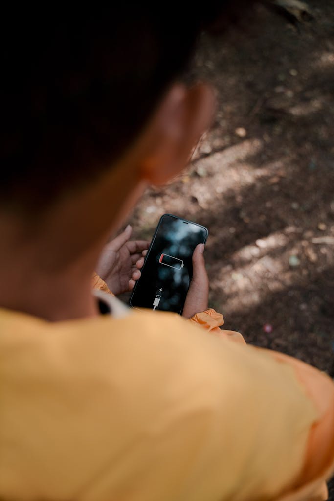 Teenager with low battery smartphone in forest reflects solitude and disconnect.