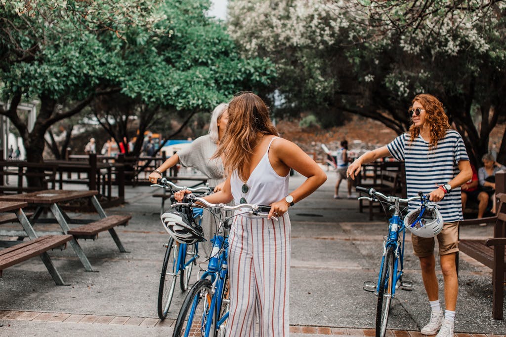Three adults enjoying a casual day with bikes in a park setting, surrounded by trees and picnic tables.