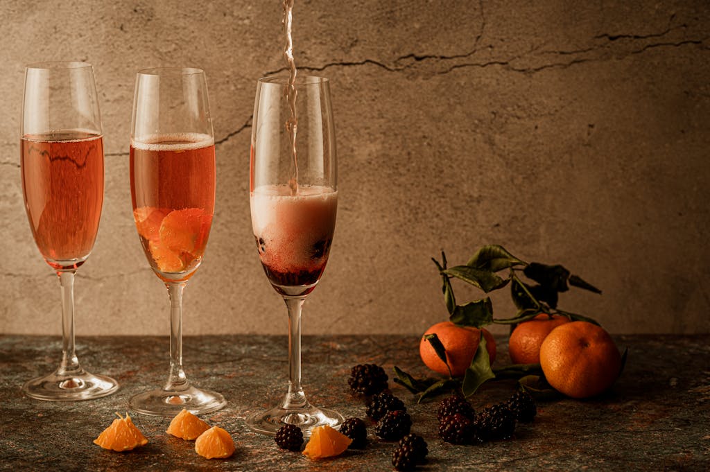 Three champagne flutes with citrus and blackberries on a moody textured surface.