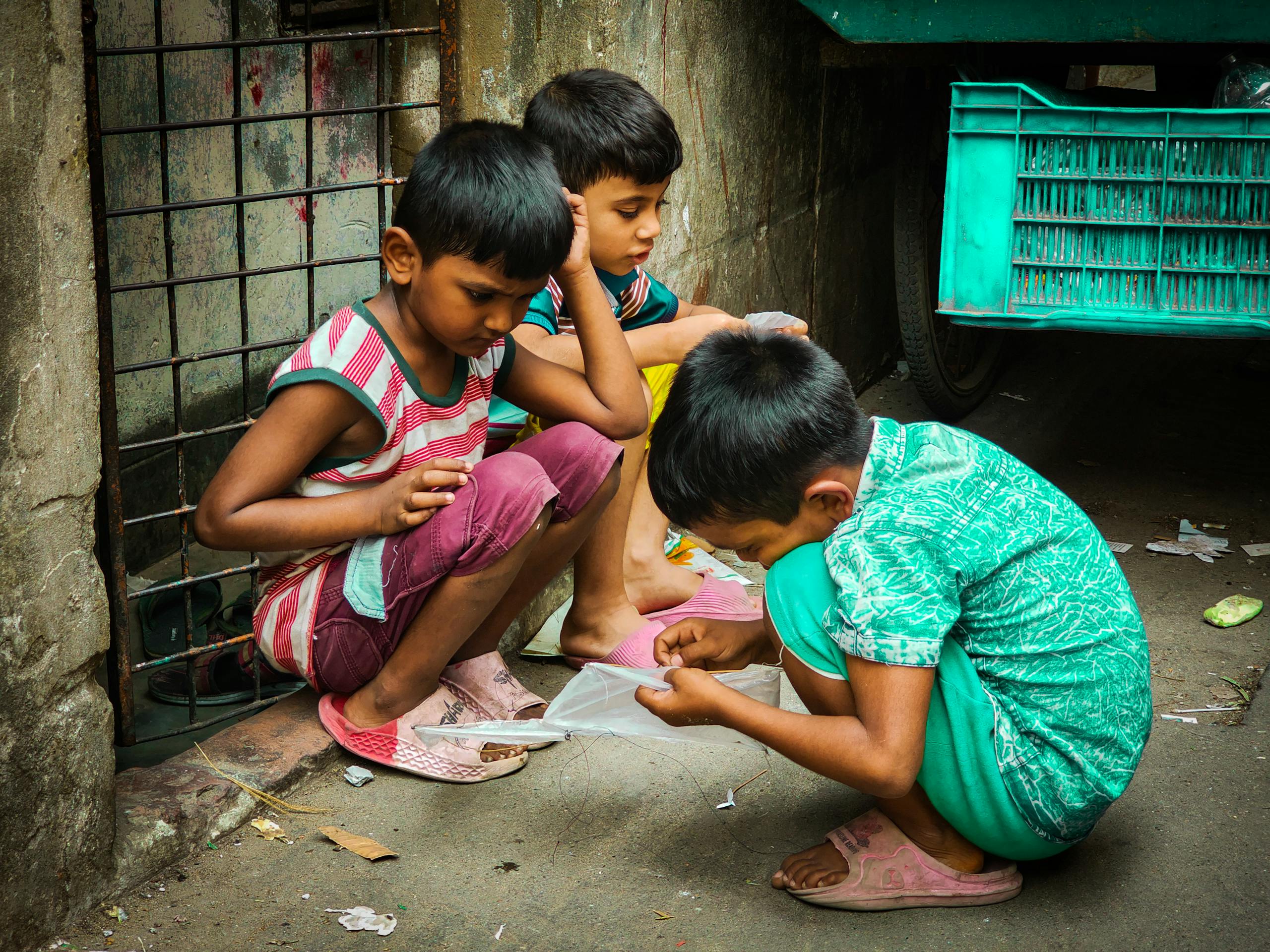 Three children engrossed in a game on a street corner, portraying simple joys of childhood.