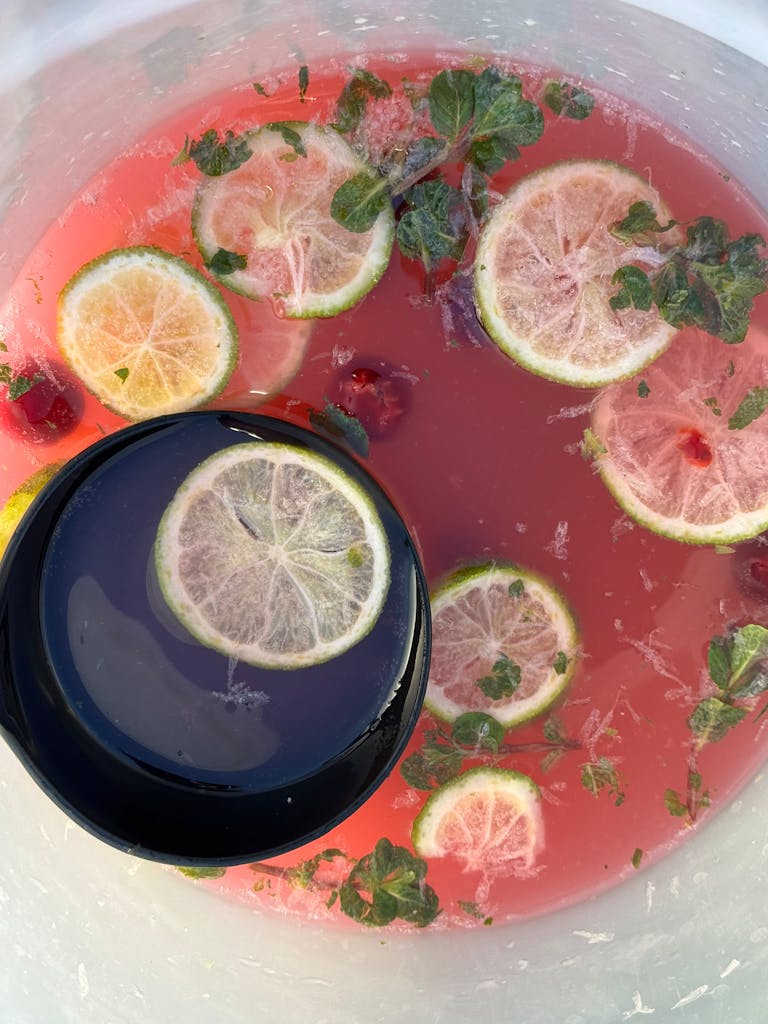 Top view of a vibrant punch bowl with lime slices, mint, and cherries, perfect for summer.