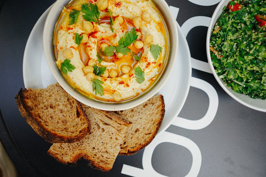 Top-view of homemade hummus garnished with parsley and served with bread slices, showcasing Mediterranean flavors.