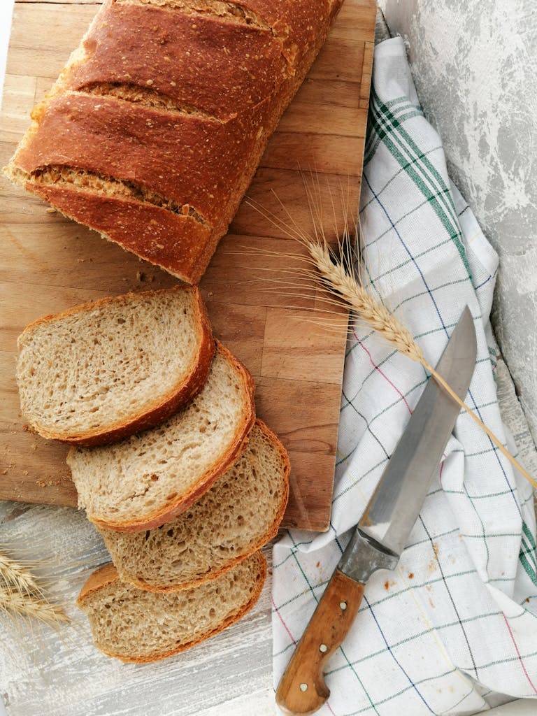 Top view of sliced wheat bread on a wooden board with a knife, showcasing rustic food styling.