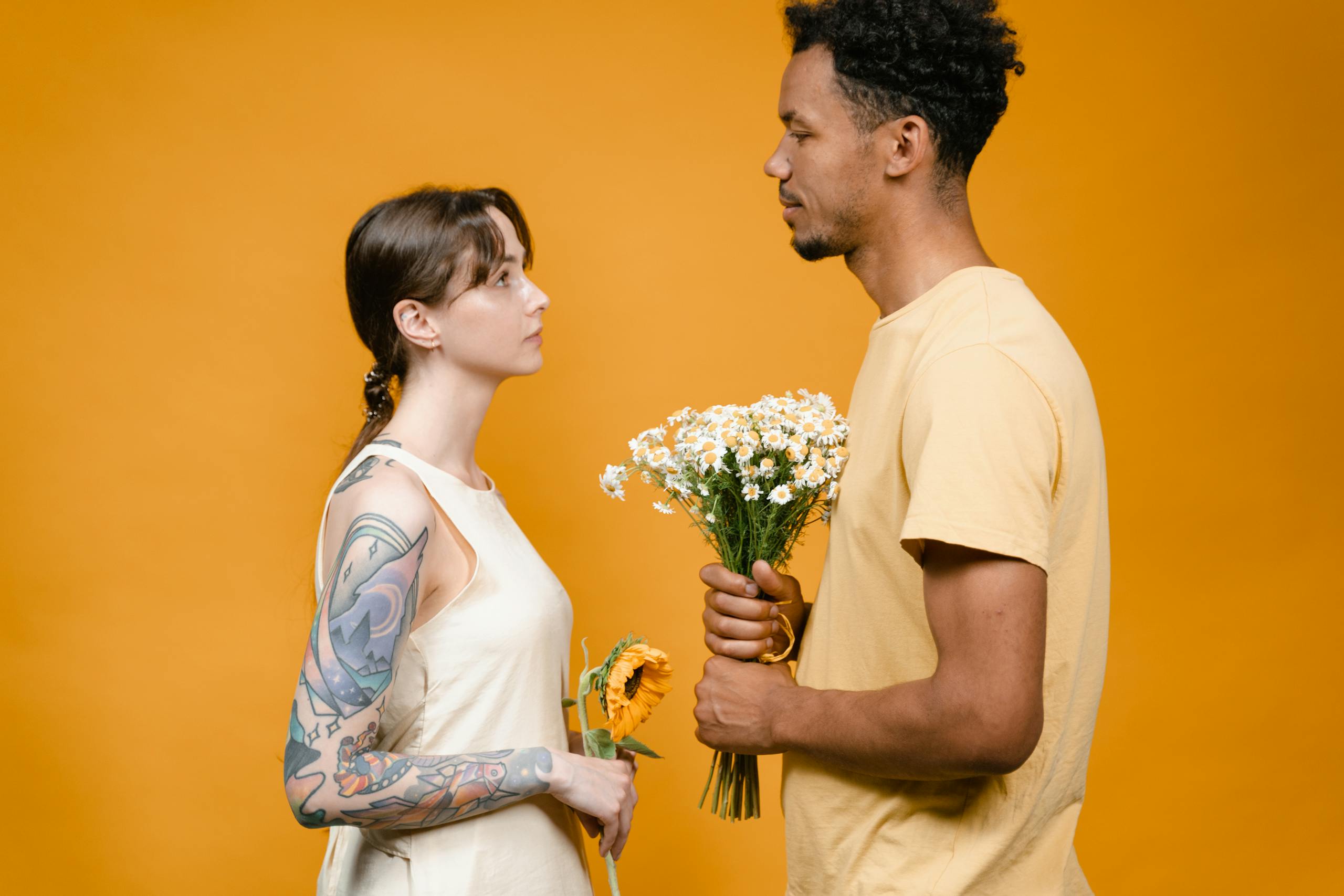 Two adults facing each other, holding flowers on a vibrant yellow background.