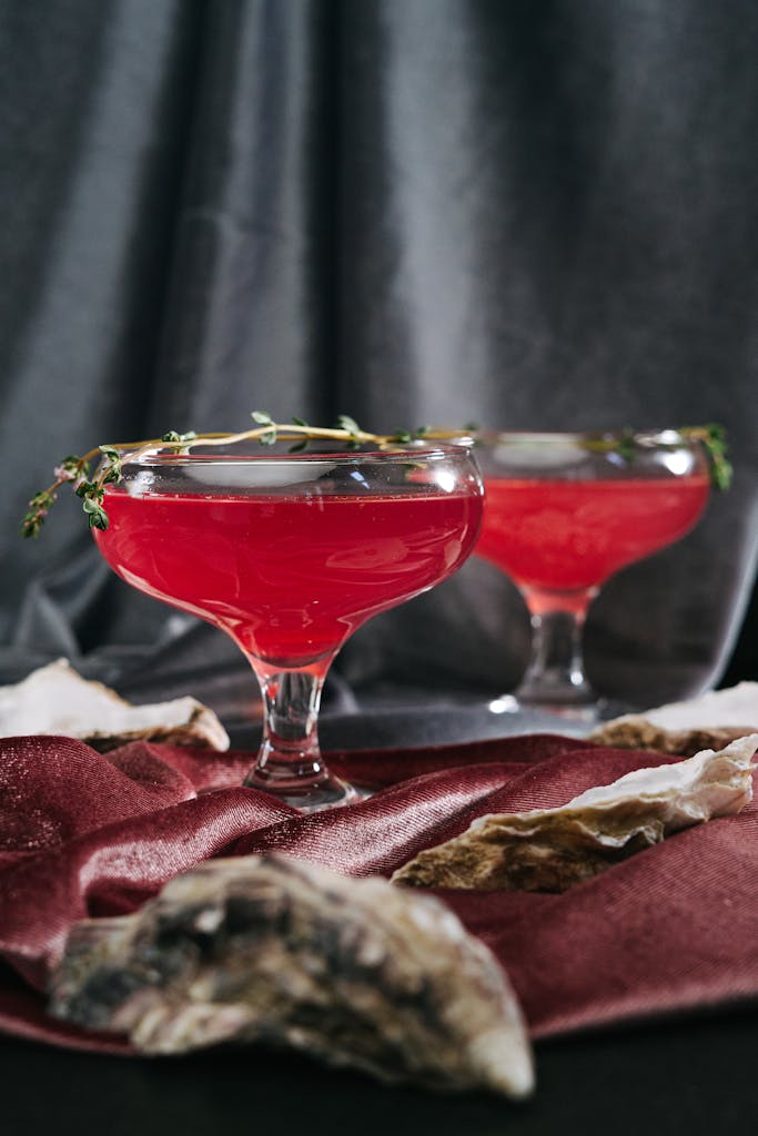 Two elegant red cocktails garnished with herbs on a luxurious velvet backdrop.