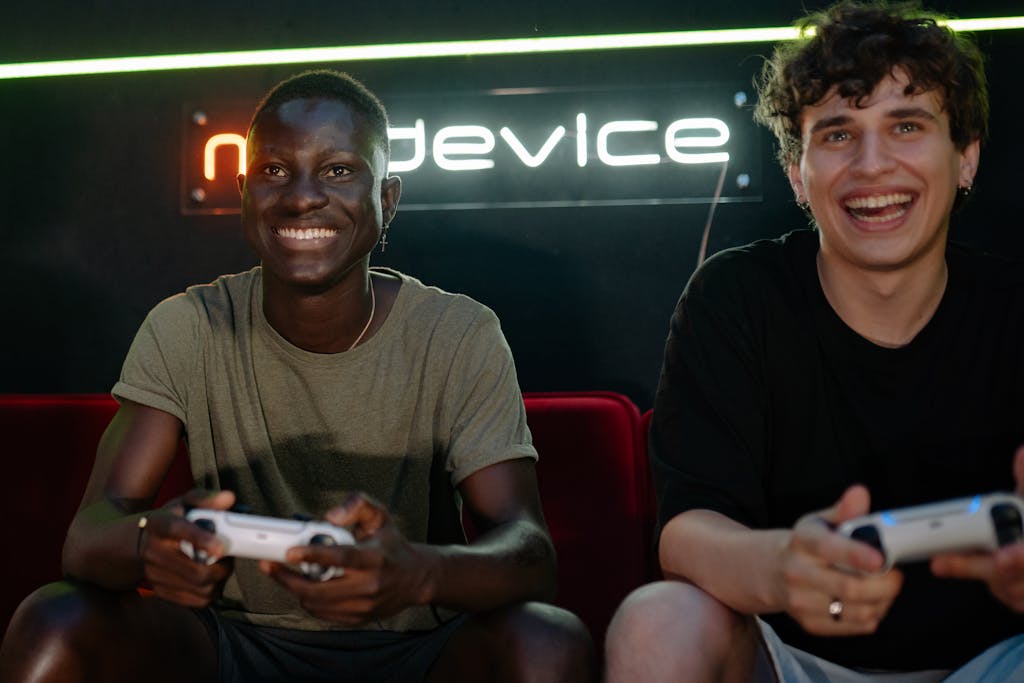 Two friends enjoying video games together indoors, smiling and holding game controllers.