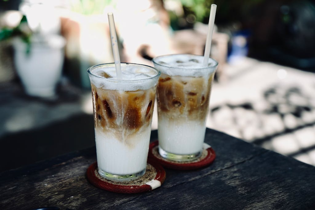Two iced coffee glasses with milk on a wooden table in an outdoor setting, perfect for summer refreshment.