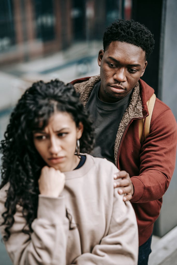 Unhappy young multiracial couple in casual clothes standing in city street while arguing with each other in daylight