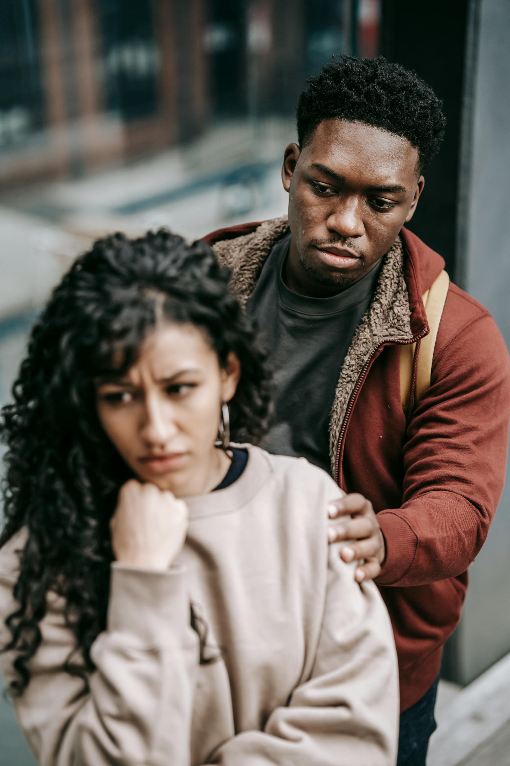 Unhappy young multiracial couple in casual clothes standing in city street while arguing with each other in daylight